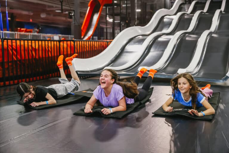 Kids laughing while racing down multi-lane slides at Sky Zone.