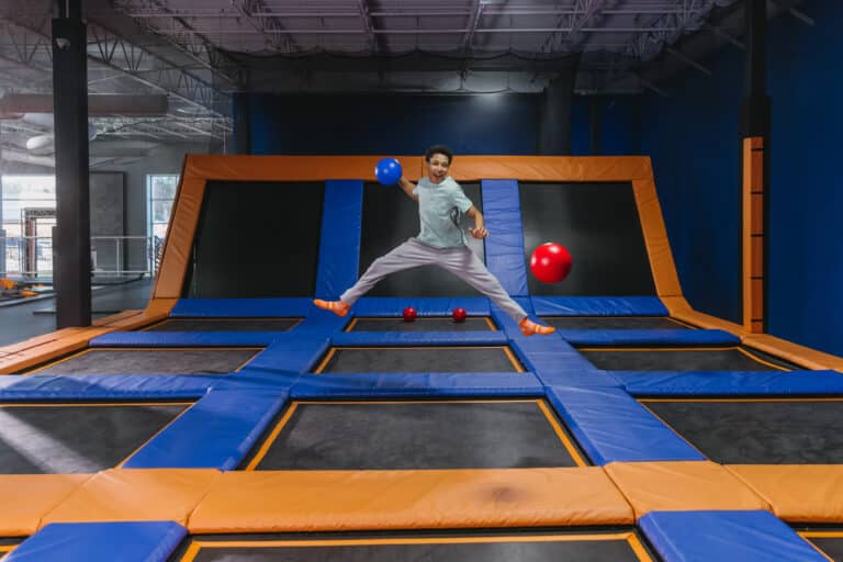 Child jumping on a trampoline while playing dodgeball at a Sky Zone indoor trampoline park.